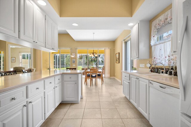 kitchen with white appliances, sink, kitchen peninsula, decorative light fixtures, and white cabinetry