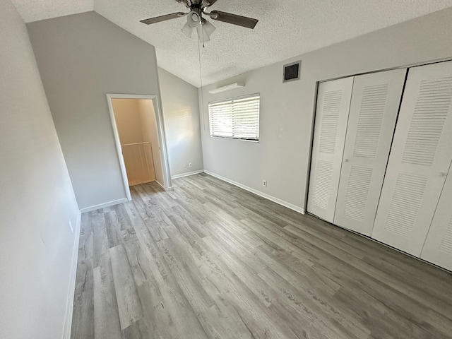 unfurnished bedroom with a closet, vaulted ceiling, a textured ceiling, and light wood-type flooring