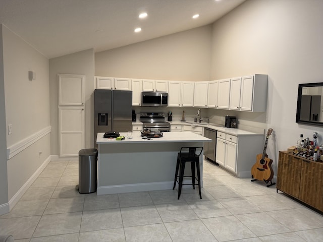 kitchen featuring appliances with stainless steel finishes, sink, light tile patterned floors, white cabinets, and a kitchen island