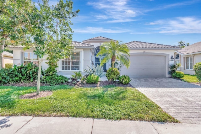 mediterranean / spanish house with a garage, a tile roof, decorative driveway, and stucco siding