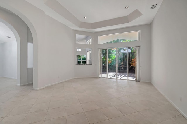 unfurnished room featuring light tile patterned floors, visible vents, baseboards, a raised ceiling, and a high ceiling