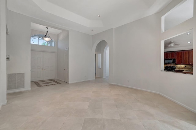 foyer entrance featuring baseboards, visible vents, arched walkways, a raised ceiling, and a high ceiling