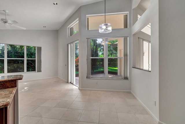 interior space featuring ceiling fan with notable chandelier, light tile patterned flooring, a towering ceiling, and baseboards