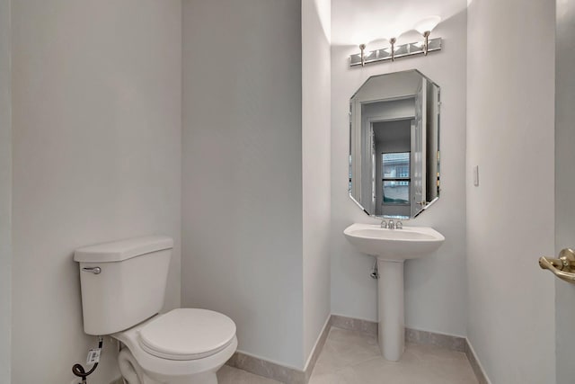 half bathroom with baseboards, toilet, and tile patterned floors