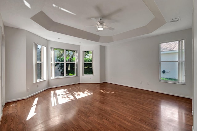 spare room featuring wood finished floors, a raised ceiling, visible vents, and a healthy amount of sunlight