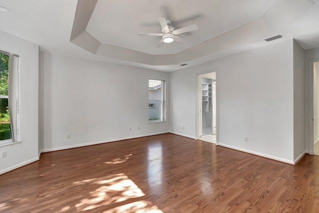 empty room featuring baseboards, visible vents, ceiling fan, wood finished floors, and a tray ceiling