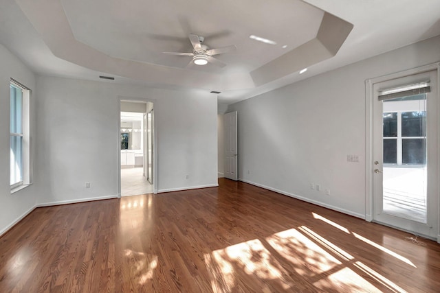 empty room featuring baseboards, wood finished floors, a raised ceiling, and a healthy amount of sunlight