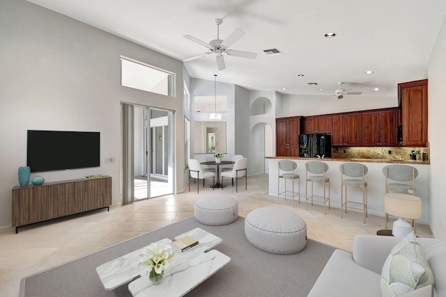 living area featuring a ceiling fan, arched walkways, visible vents, and light tile patterned floors