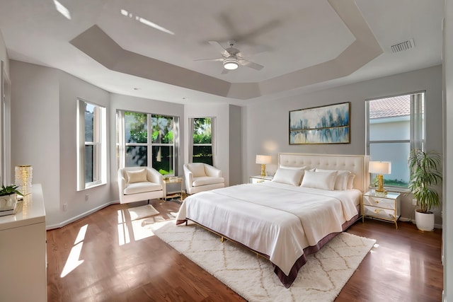 bedroom with baseboards, visible vents, a ceiling fan, wood finished floors, and a tray ceiling