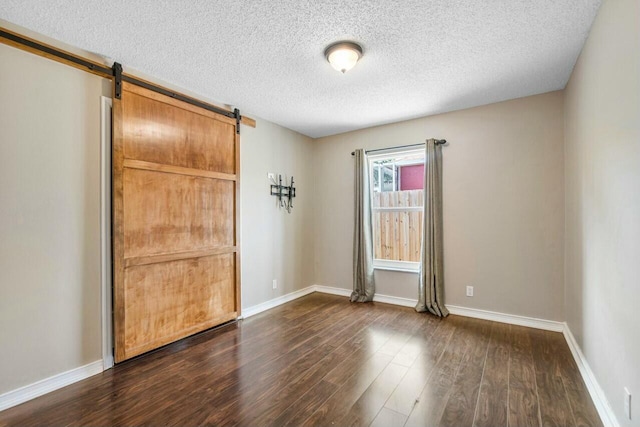 spare room featuring a textured ceiling, a barn door, and dark hardwood / wood-style floors