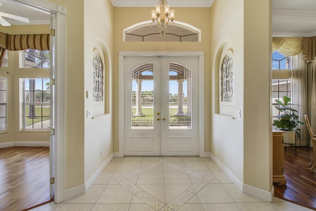 tiled entryway featuring ceiling fan with notable chandelier, crown molding, a wealth of natural light, and french doors