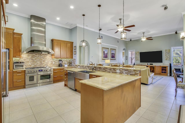 kitchen with wall chimney range hood, sink, light tile patterned floors, appliances with stainless steel finishes, and decorative light fixtures