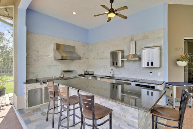 kitchen with wall chimney exhaust hood, decorative backsplash, sink, and a breakfast bar area