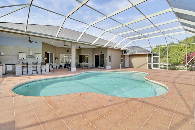 view of swimming pool with glass enclosure, ceiling fan, exterior bar, and a patio