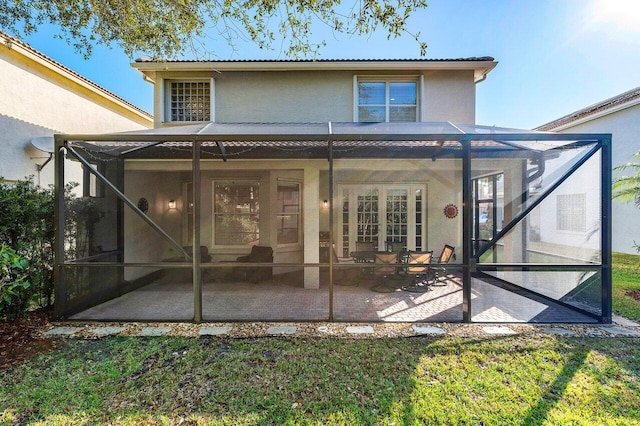 back of property featuring a lawn, glass enclosure, and a patio