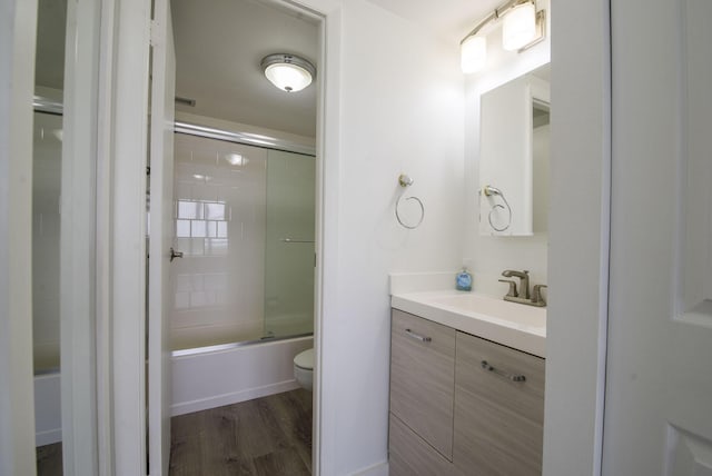 full bathroom featuring toilet, vanity, wood finished floors, and bath / shower combo with glass door