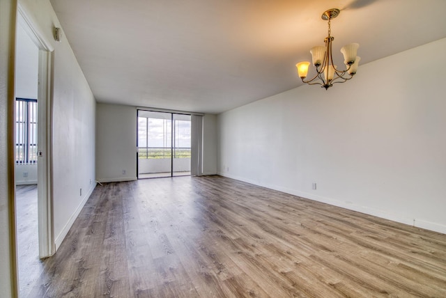 empty room with wood finished floors, a chandelier, baseboards, and expansive windows