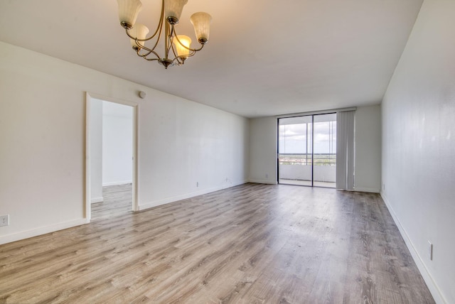 empty room with a notable chandelier, expansive windows, and light hardwood / wood-style flooring