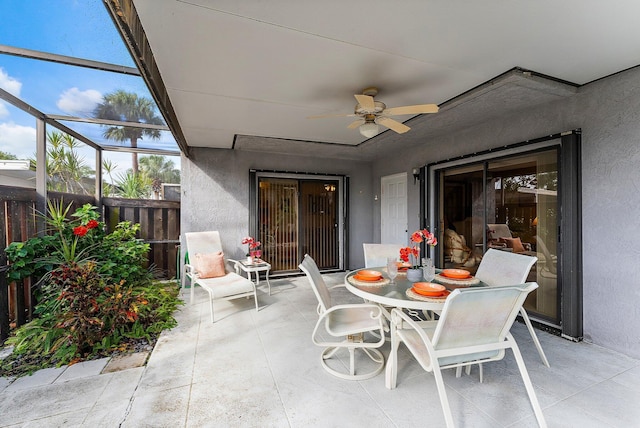 view of patio featuring glass enclosure, outdoor dining space, fence, and a ceiling fan