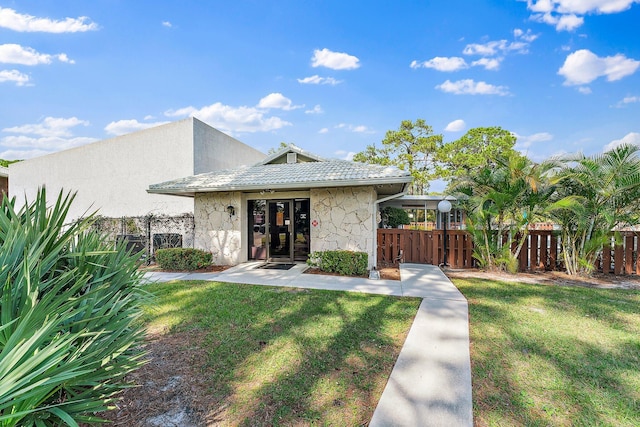 view of front of house with stone siding, a front yard, fence, and a tile roof