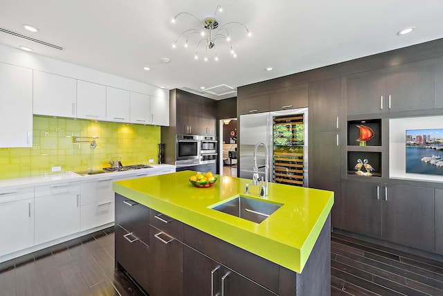 kitchen featuring white cabinetry, a center island with sink, stainless steel appliances, dark brown cabinetry, and sink