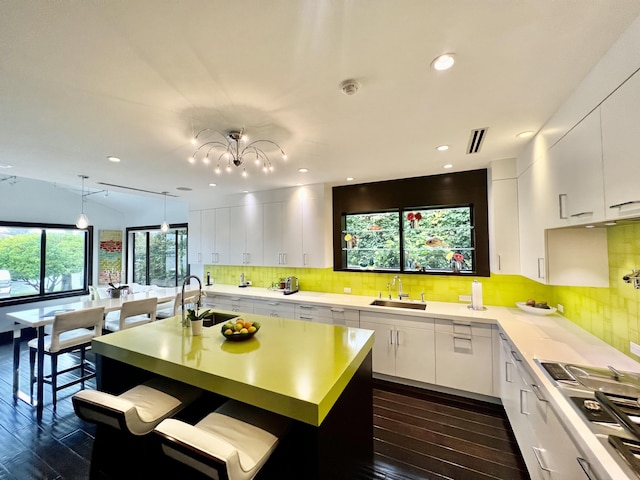 kitchen featuring light countertops, dark wood-type flooring, white cabinetry, a sink, and an island with sink