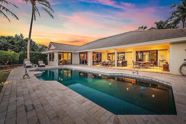 pool at dusk with a patio area and outdoor lounge area