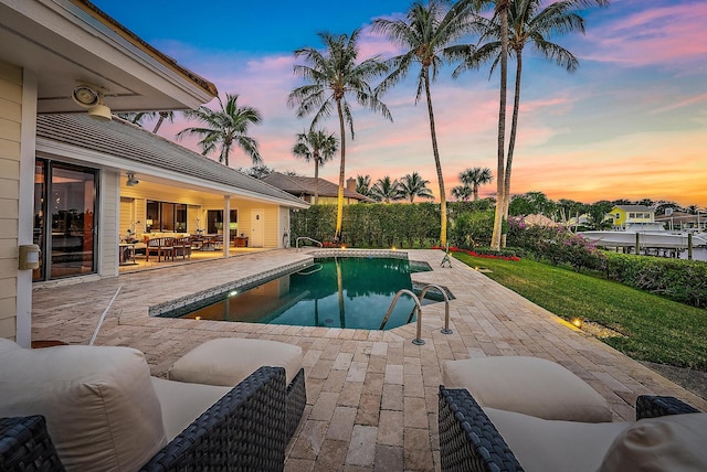 pool at dusk with a patio area and a yard