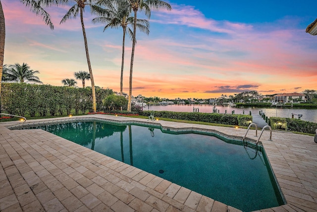 pool at dusk featuring a water view and a patio area