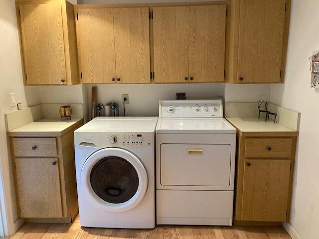 laundry area with cabinets, light hardwood / wood-style flooring, and washing machine and clothes dryer