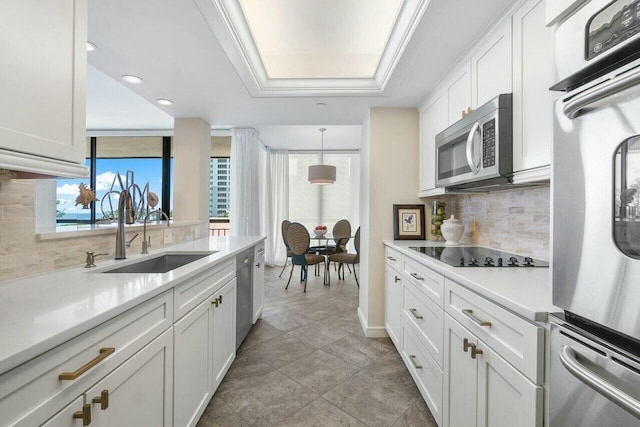 kitchen with pendant lighting, white cabinetry, stainless steel appliances, sink, and a tray ceiling