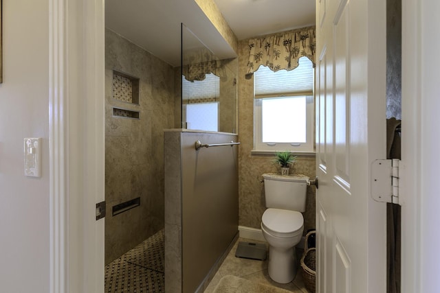 bathroom featuring tile patterned flooring, toilet, and tiled shower