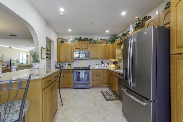 kitchen with a center island, a textured ceiling, decorative backsplash, a breakfast bar, and appliances with stainless steel finishes