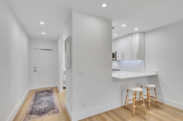 kitchen featuring kitchen peninsula, white cabinetry, a breakfast bar area, and light hardwood / wood-style flooring