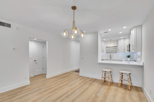 kitchen featuring white cabinetry, kitchen peninsula, light hardwood / wood-style floors, decorative light fixtures, and a kitchen bar