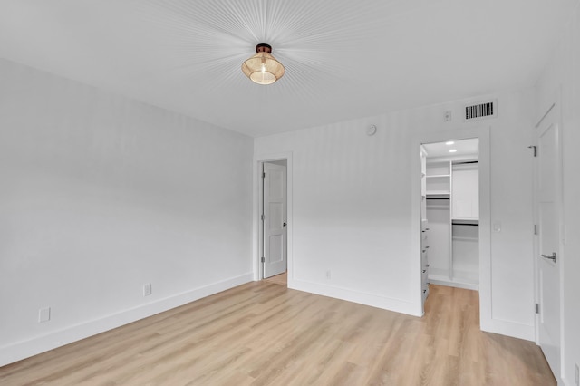 unfurnished bedroom featuring light wood-type flooring, a walk in closet, and a closet