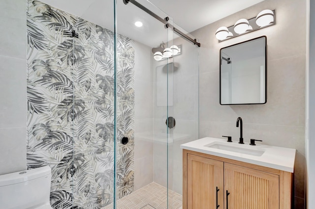 bathroom featuring vanity, a shower with door, toilet, and tile walls