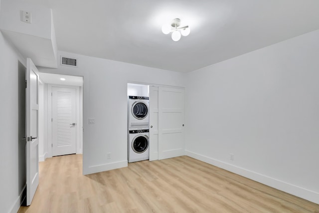 laundry area with stacked washing maching and dryer and light hardwood / wood-style floors