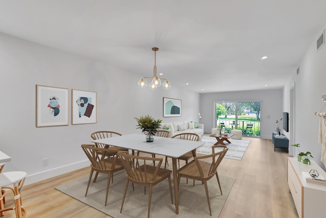 dining area with light wood-type flooring and an inviting chandelier