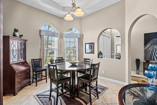 dining space with light tile patterned floors, ornamental molding, and a tray ceiling