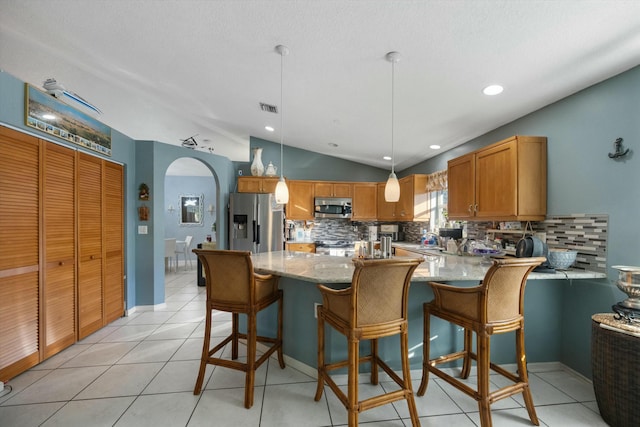 kitchen featuring pendant lighting, appliances with stainless steel finishes, tasteful backsplash, vaulted ceiling, and light stone counters