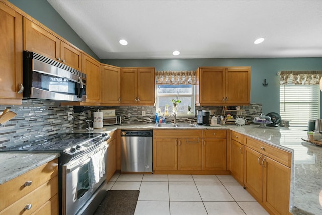 kitchen with a wealth of natural light, appliances with stainless steel finishes, light stone counters, and sink