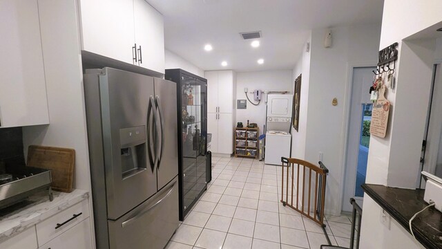 kitchen with white cabinetry, stacked washer / dryer, stainless steel fridge, and light tile patterned floors