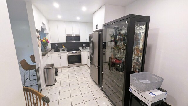 kitchen featuring backsplash, light tile patterned floors, stainless steel appliances, and white cabinets