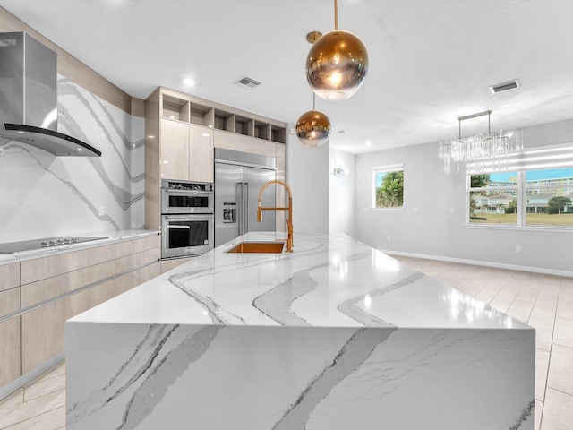 kitchen with decorative light fixtures, appliances with stainless steel finishes, wall chimney exhaust hood, and light stone countertops