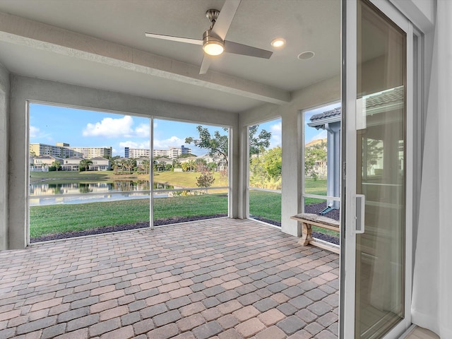 unfurnished sunroom featuring ceiling fan and a water view