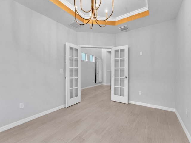 spare room featuring a raised ceiling, crown molding, light wood-type flooring, french doors, and a chandelier