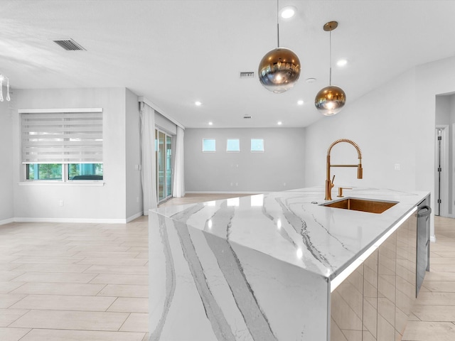 kitchen with an island with sink, light stone counters, hanging light fixtures, and sink