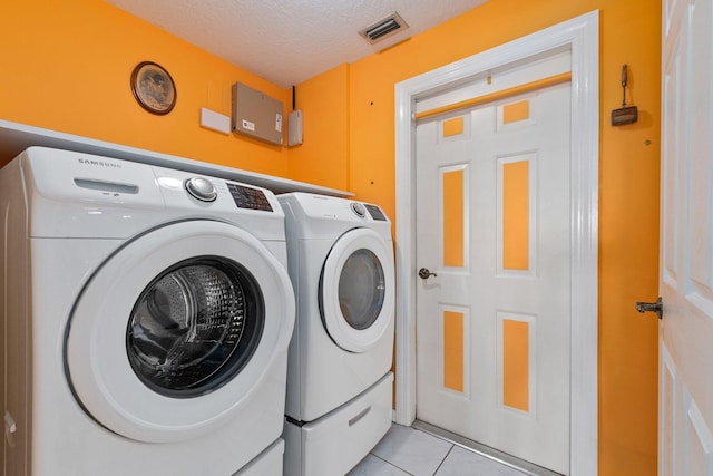 clothes washing area with washer and dryer, light tile patterned floors, and a textured ceiling