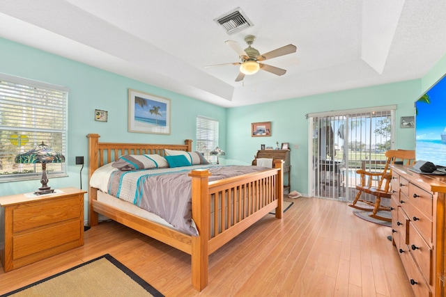 bedroom featuring a tray ceiling, access to exterior, ceiling fan, and light wood-type flooring